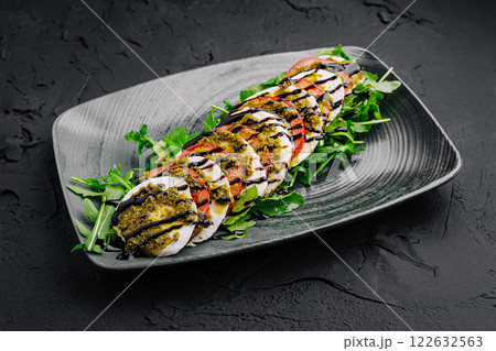 Freshly prepared salad with pesto, grilled vegetables, and arugula served on a sleek black plate 122632563