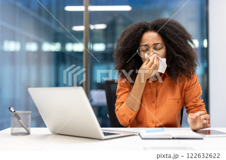 Woman in office sneezing at desk using tissue, illustrating cold symptoms and health awareness. Concept of work during illness and need for self-care in professional setting. Woman in office sneezing at desk using tissue, illustrating cold symptoms and health awareness. Concept of work during illness and need for self-care in professional setting. 122632622