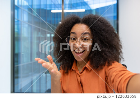 Happy young woman takes selfie with phone in modern office, displaying joy and connection. Bright smile and engaging expression capture positive communication. Happy young woman takes selfie with phone in modern office, displaying joy and connection. Bright smile and engaging expression capture positive communication. 122632659