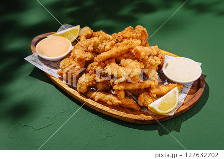 Crispy fried seafood platter served with dipping sauces and lemon wedges at a sunny outdoor table 122632702