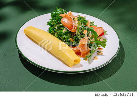 Delicious omelette served with fresh salad featuring kale and smoked salmon at a cozy dining setting 122632711