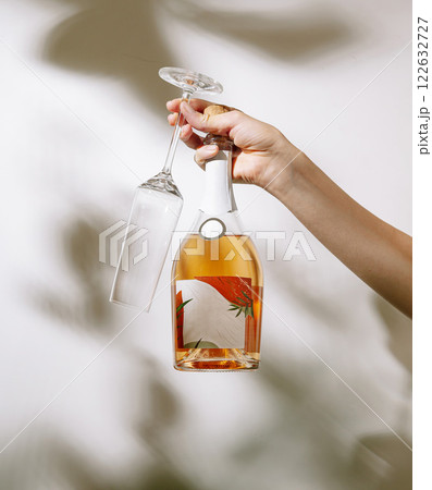 Hand holding a bottle of rose wine and an empty glass with a floral label in soft lighting Hand holding a bottle of rose wine and an empty glass with a floral label in soft lighting 122632727