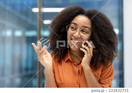 Smiling woman having phone conversation in modern office. Wearing glasses and orange shirt, appears happy, engaged, showcasing concept of communication, connection, technology, and business setting. Smiling woman having phone conversation in modern office. Wearing glasses and orange shirt, appears happy, engaged, showcasing concept of communication, connection, technology, and business setting. 122632731