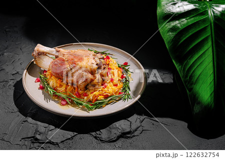 Savory meat dish garnished with pomegranate and herbs on a rustic plate with green foliage 122632754