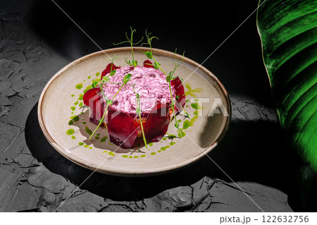 Delicate beetroot dish with herbs and sauce presented elegantly on a textured plate in a dimly lit setting 122632756