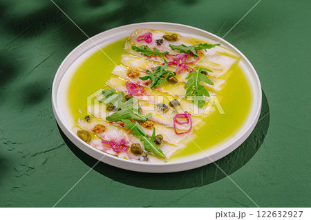 Ceviche served on a white plate presents fresh fish with vibrant garnish and green sauce on a striking green background 122632927