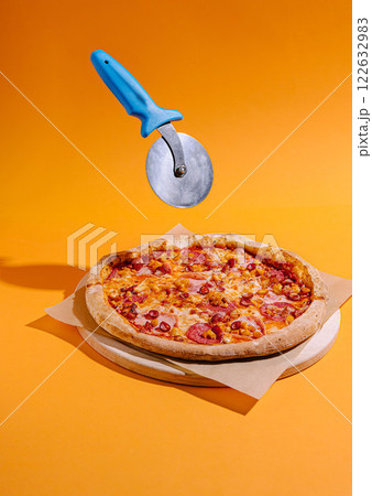 Pizza with vibrant orange background and a pizza cutter floating above ready for slicing 122632983