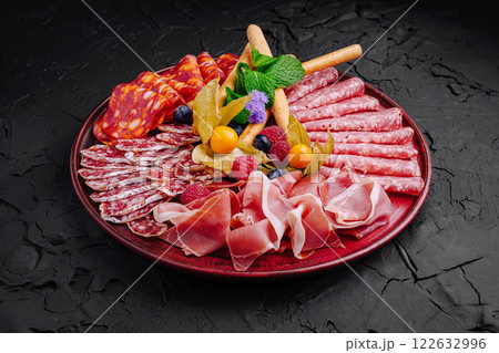 Cured meats and fruits arranged beautifully on a dark platter for a gourmet presentation 122632996