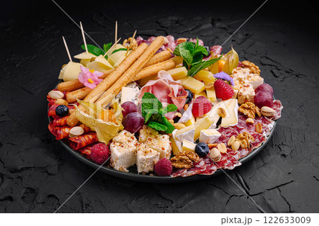 Exquisite charcuterie platter featuring a variety of cheeses, meats, fruits, and nuts displayed elegantly for a festive gathering Exquisite charcuterie platter featuring a variety of cheeses, meats, fruits, and nuts displayed elegantly for a festive gathering 122633009
