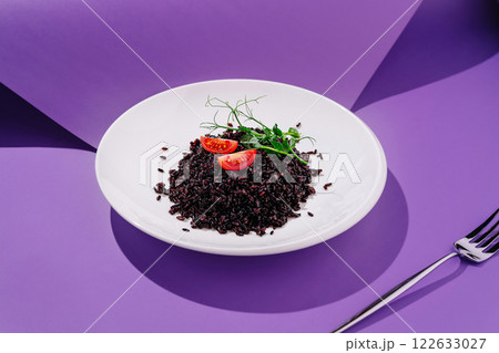 Delicious black rice dish garnished with fresh tomatoes and herbs on a vibrant purple background Delicious black rice dish garnished with fresh tomatoes and herbs on a vibrant purple background 122633027