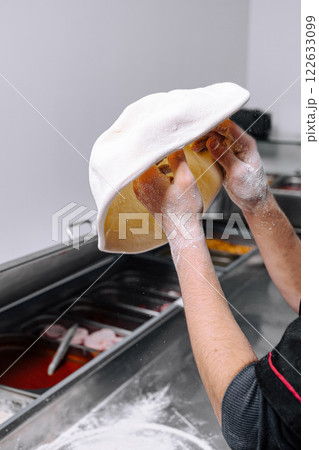 Chef skillfully tossing pizza dough in a bustling kitchen during the lunch rush 122633099