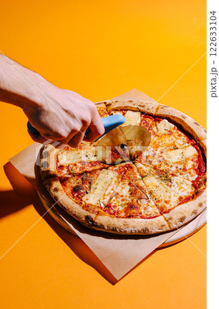 Delicious pizza being cut with a circular cutter on a vibrant yellow background Delicious pizza being cut with a circular cutter on a vibrant yellow background 122633104