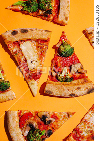Colorful assortment of pizza slices with vegetables arranged on a vibrant orange background 122633105