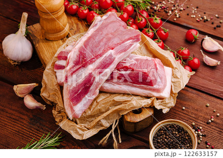 Fresh pork ribs with tomatoes, garlic, and herbs arranged on a wooden table for a home cooking preparation 122633157
