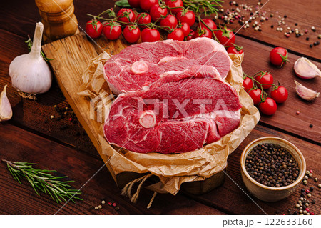 Fresh cuts of meat laid on a wooden board surrounded by herbs and vegetables at a rustic kitchen setting Fresh cuts of meat laid on a wooden board surrounded by herbs and vegetables at a rustic kitchen setting 122633160