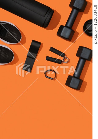 Black exercise equipment, dumbbells, mat, elastic band, fitness band, fitness band, sneakers on orange background. Fitness, sports items, healthy lifestyle. Place for your text Black exercise equipment, dumbbells, mat, elastic band, fitness band, fitness band, sneakers on orange background. Fitness, sports items, healthy lifestyle. Place for your text 122633419