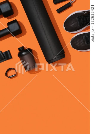 Vertical banner with black workout equipment, dumbbells, mat, sneakers, bottle, hand grip on orange background. Fitness, sports items, healthy lifestyle concept. Space for your text 122633421
