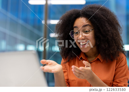Happy woman in glasses interacting during online meeting on laptop, showing confident and positive attitude. Expressive body language reflects engagement and enthusiasm. Happy woman in glasses interacting during online meeting on laptop, showing confident and positive attitude. Expressive body language reflects engagement and enthusiasm. 122633580