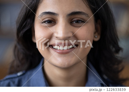 Close-up portrait of a happy young brunette Indian woman in a denim shirt smiling at the camera. 122633839