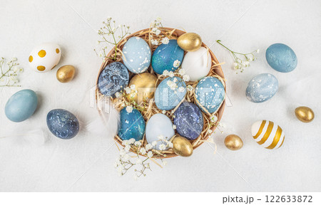 Basket with painted Easter eggs on white background surrounded by flowers. Stylish golden and blue eggs. top view Basket with painted Easter eggs on white background surrounded by flowers. Stylish golden and blue eggs. top view 122633872