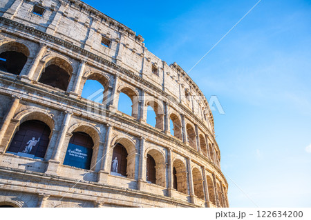 Visitors admire the grand structure of the Colosseum in Rome, Italy, showcasing its impressive ancient architecture against a clear blue sky, highlighting its historical significance and beauty. 122634200