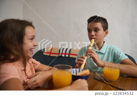 Young boy playing flute while girl laughs during a light meal Young boy playing flute while girl laughs during a light meal 122634532