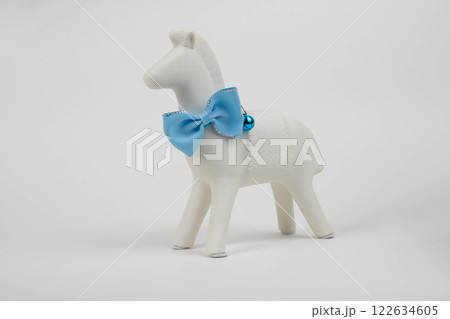 A white horse with a blue collar with a bow and a bell stands on the table 122634605
