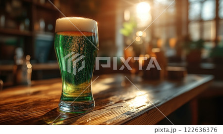 Foamy green beer glass placed on rustic wooden table in cozy, sunlit pub. 122636376