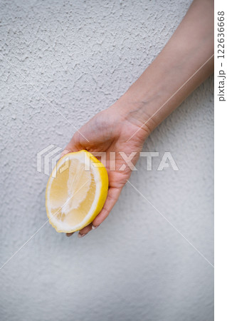 Woman hand holding halved lemon on white wall background Woman hand holding halved lemon on white wall background 122636668