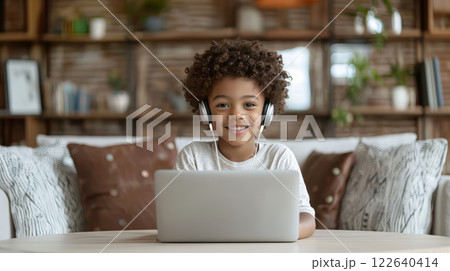Smiling haired curly african american schoolboy 12 years old engaged in online learning with laptop and headphones at home. Childhood and technology. 122640414