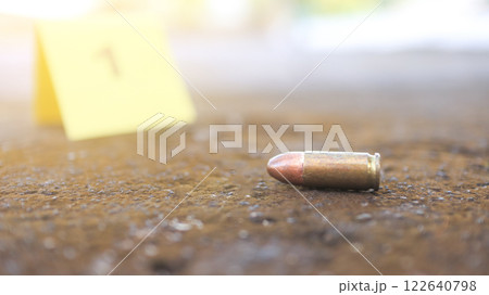 A spent bullet casing in focus, with a blurred forensic number 1 tag behind it, symbolizes crime scene investigation, evidence collection, and law enforcement efforts in forensic science. 122640798