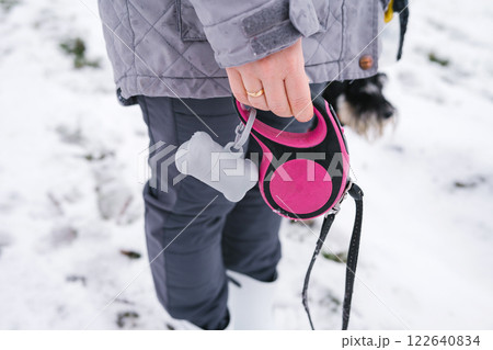 Close-up of person holding retractable dog leash in snowy winter scene. International Pooper Scooper Week Close-up of person holding retractable dog leash in snowy winter scene. International Pooper Scooper Week 122640834