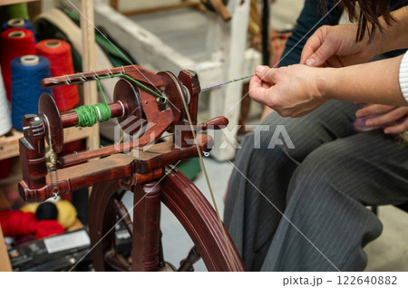 Distaff Day Close-up of adult spinning yarn on traditional spinning wheel Distaff Day Close-up of adult spinning yarn on traditional spinning wheel 122640882