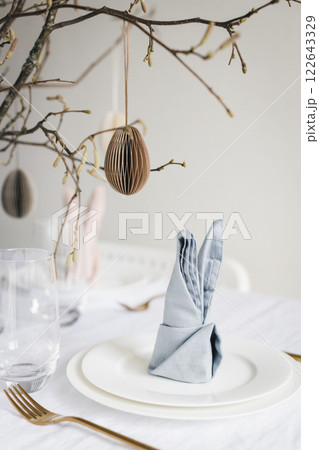 Easter table setting with bunny ear napkins and paper eggs hanging on branches. 122643329