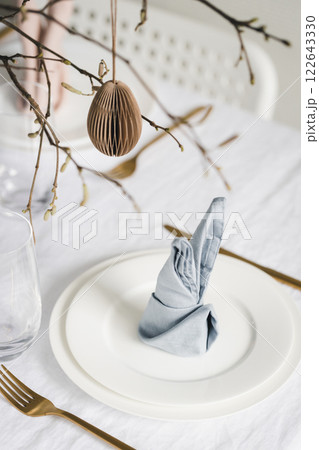 Easter table setting with bunny ear napkins and paper eggs hanging on branches. Easter table setting with bunny ear napkins and paper eggs hanging on branches. 122643330