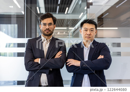 Two business professionals stand confidently with arms crossed in modern office, highlighting concepts of leadership, determination, and teamwork. Ideal representation of corporate atmosphere Two business professionals stand confidently with arms crossed in modern office, highlighting concepts of leadership, determination, and teamwork. Ideal representation of corporate atmosphere 122644080