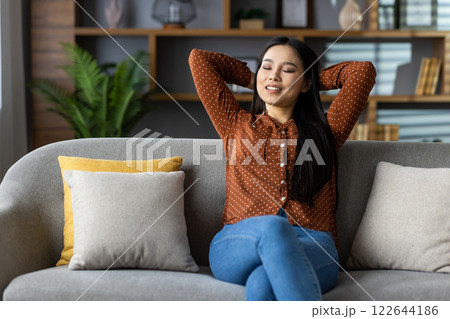 Asian woman relaxing on sofa in modern living room, embracing contentment and serenity. Experience peaceful moment in home comfort with casual style. Asian woman relaxing on sofa in modern living room, embracing contentment and serenity. Experience peaceful moment in home comfort with casual style. 122644186