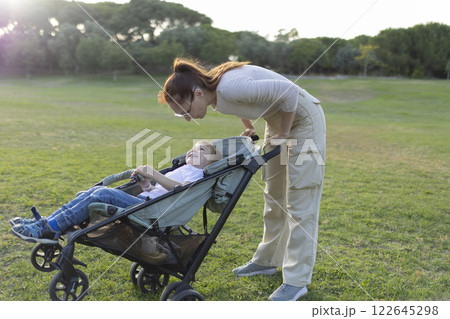 Mother talking with her son sitting in a stroller in a park 122645298