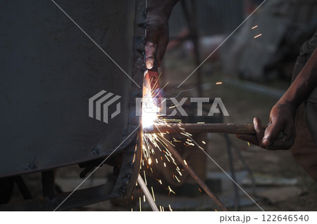 Worker welding metal structure at a construction site in evening light 122646540