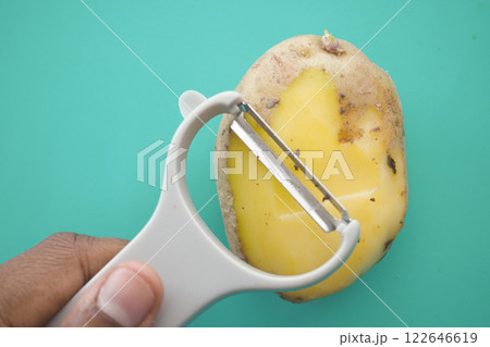 Potato peeling activity on a bright turquoise cutting board by a hand holding a peeler Potato peeling activity on a bright turquoise cutting board by a hand holding a peeler 122646619