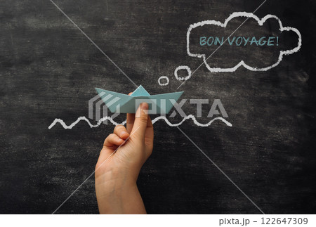 A hand holding a paper boat in a chalkboard with the words Bon Voyage 122647309