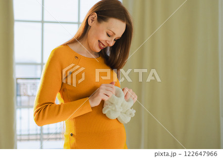 Pregnancy motherhood people expectation future. Pregnant woman with big belly holding newborn baby booties smiling at home. Young mom enjoying pregnancy. Maternity tenderness parenthood new life 122647966