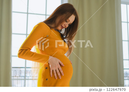 Pregnancy motherhood people expectation future. Pregnant woman with big belly standing near window at home. Girl hugging her tummy enjoying pregnancy. Maternity tenderness parenthood new life concept Pregnancy motherhood people expectation future. Pregnant woman with big belly standing near window at home. Girl hugging her tummy enjoying pregnancy. Maternity tenderness parenthood new life concept 122647970
