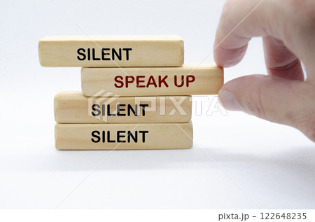 Hand pulling out wooden block with text saying SPEAK UP to separate from other wooden blocks with text SILENT. Courage and Speak Up concept. 122648235