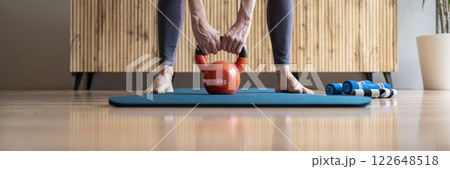 Fit woman holding an 8 kilogram kettlebell weight between her legs 122648518