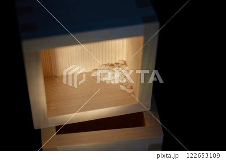 スポットライトに照らされた升に残った少量のコメ 122653109