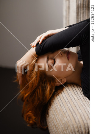 Elegant redhead woman with long hair leaning back in chair looking at camera Elegant redhead woman with long hair leaning back in chair looking at camera 122654123