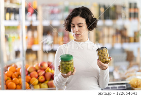 In store, woman near counter are looking at pickled green olives jar 122654643