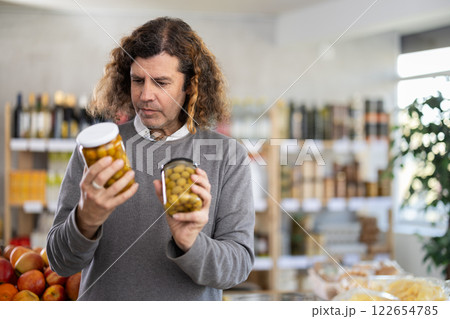 Male shopper choosing canned green olives in supermarket Male shopper choosing canned green olives in supermarket 122654785