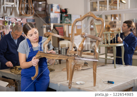 Young female furniture maker working on vintage chair in workshop Young female furniture maker working on vintage chair in workshop 122654985